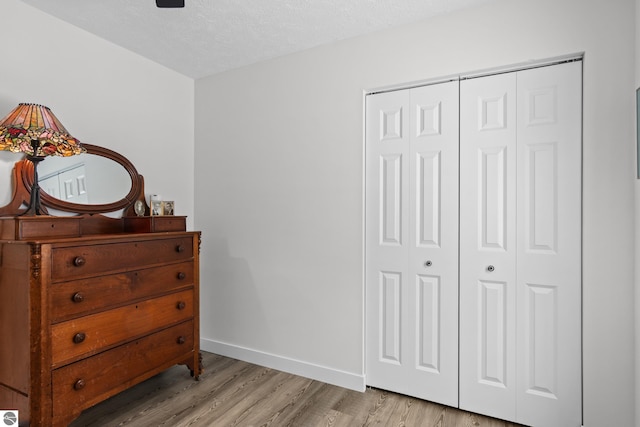 bedroom featuring a closet, light wood-style flooring, baseboards, and a textured ceiling