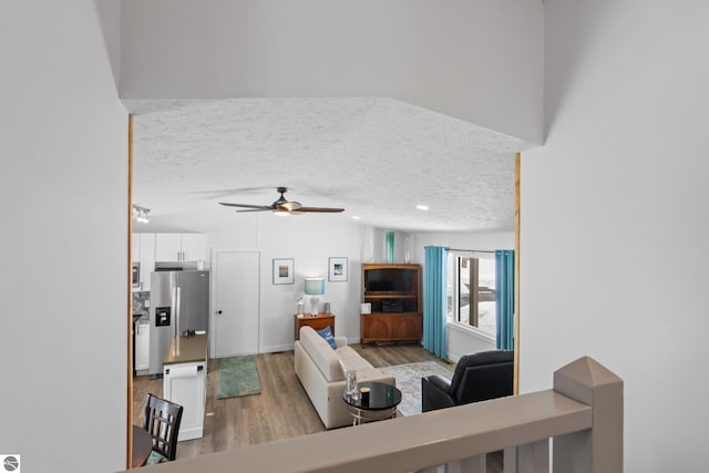 living room featuring a textured ceiling, ceiling fan, light wood finished floors, and vaulted ceiling