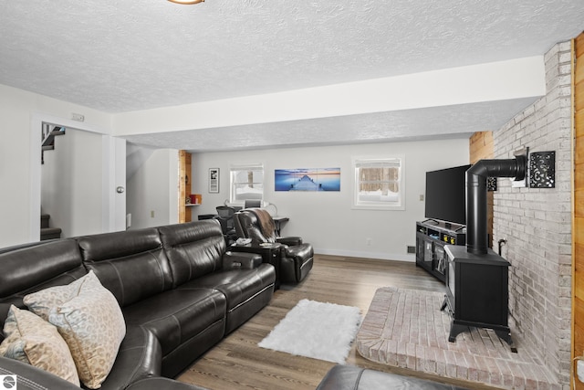 living room featuring stairway, a wood stove, a textured ceiling, wood finished floors, and baseboards