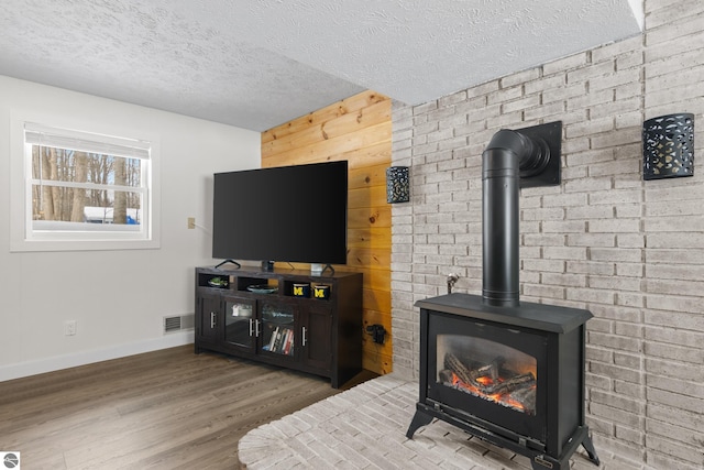 living room featuring visible vents, a wood stove, a textured ceiling, wood finished floors, and baseboards