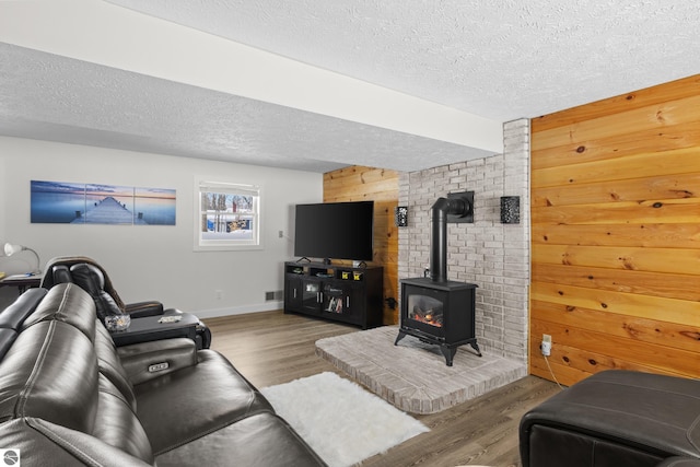 living area with a wood stove, wood walls, a textured ceiling, and wood finished floors