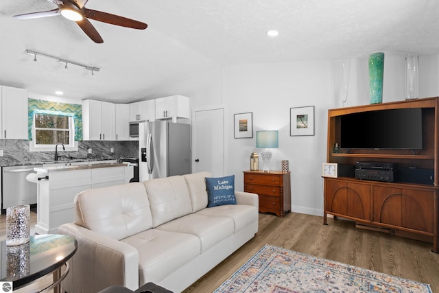 living room with a textured ceiling, wood finished floors, a ceiling fan, baseboards, and vaulted ceiling