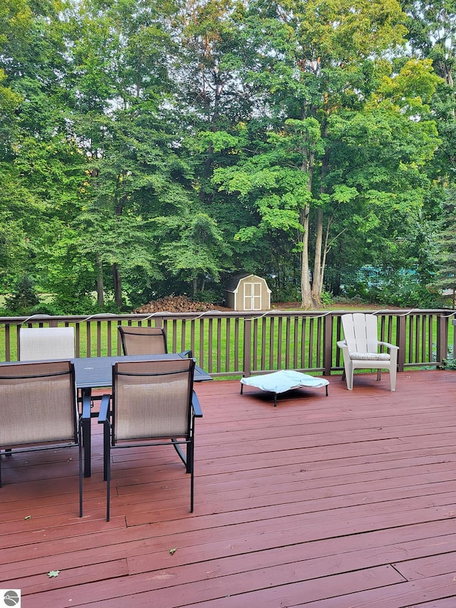 wooden deck featuring a yard, outdoor dining area, an outdoor structure, and a shed