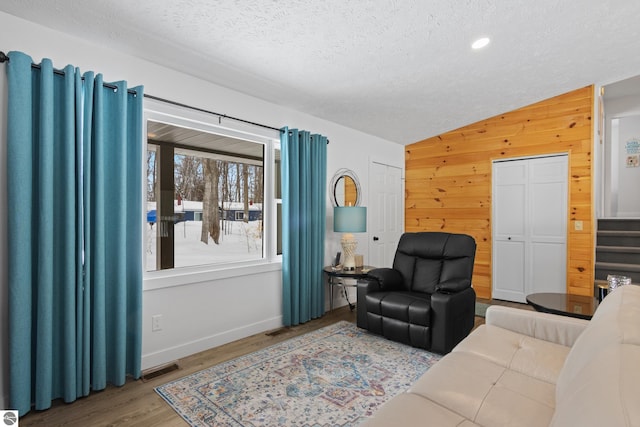 living area with visible vents, vaulted ceiling, a textured ceiling, light wood-type flooring, and wood walls