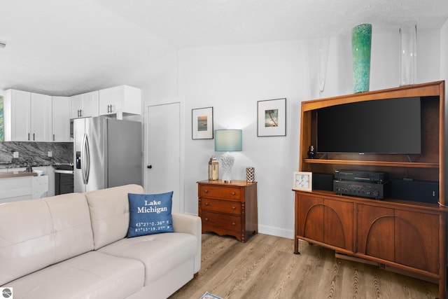 living area with vaulted ceiling, light wood finished floors, and baseboards