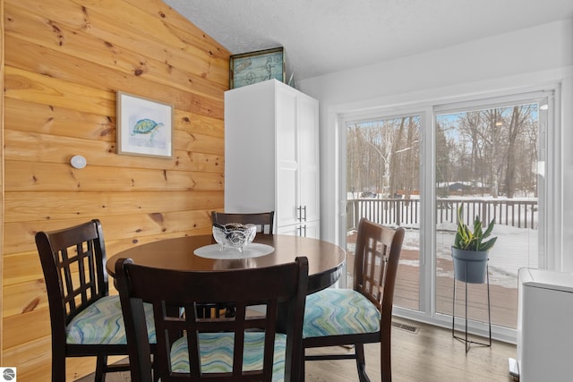 dining space with a textured ceiling, wooden walls, visible vents, and wood finished floors