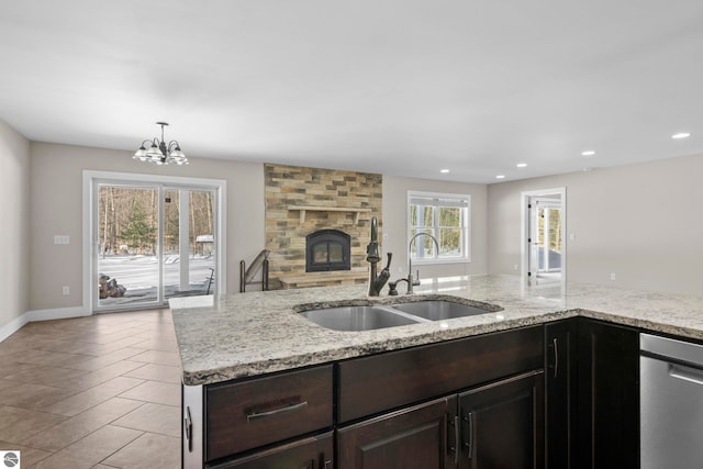 kitchen with light stone counters, a fireplace, a sink, dark brown cabinets, and dishwasher