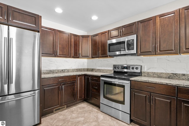 kitchen with stainless steel appliances, dark brown cabinets, light stone counters, and decorative backsplash