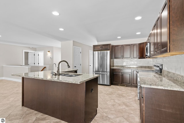 kitchen featuring dark brown cabinetry, a sink, a kitchen island with sink, stainless steel appliances, and backsplash