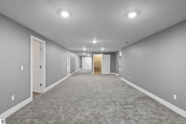 finished below grade area with a barn door, carpet flooring, and baseboards