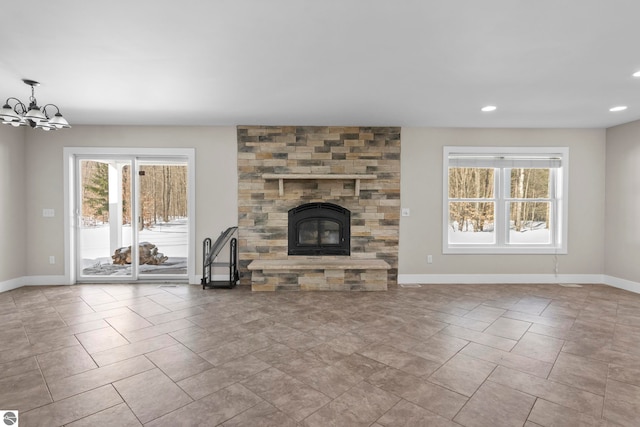 unfurnished living room featuring a notable chandelier, a fireplace, baseboards, and a wealth of natural light