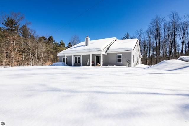 snow covered back of property featuring a garage and a chimney