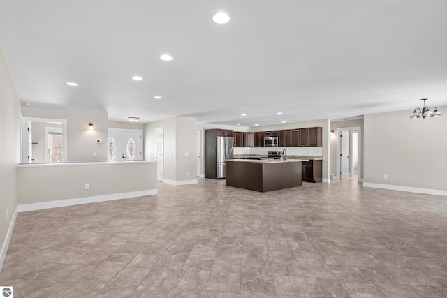 kitchen with a chandelier, a kitchen island with sink, stainless steel appliances, open floor plan, and dark brown cabinets