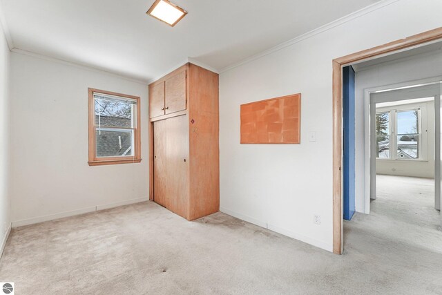 unfurnished bedroom featuring a closet, baseboards, crown molding, and light colored carpet
