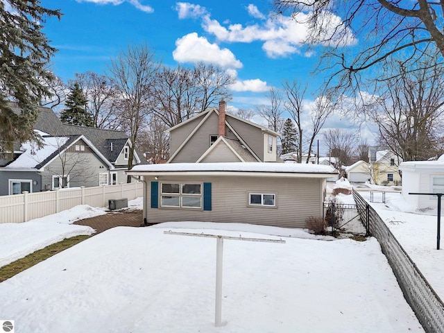 snow covered property featuring central AC unit, a chimney, fence, and a residential view