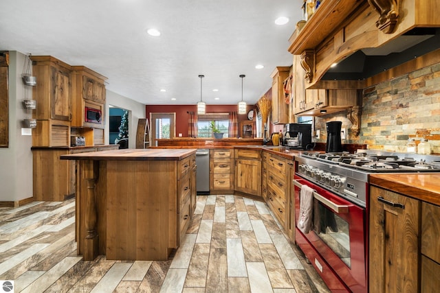 kitchen with dark countertops, appliances with stainless steel finishes, hanging light fixtures, range hood, and a kitchen bar