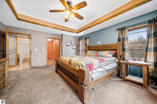 bedroom with a raised ceiling, light colored carpet, baseboards, and ensuite bathroom