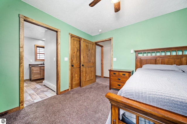 bedroom featuring a baseboard heating unit, baseboards, ensuite bathroom, and light colored carpet