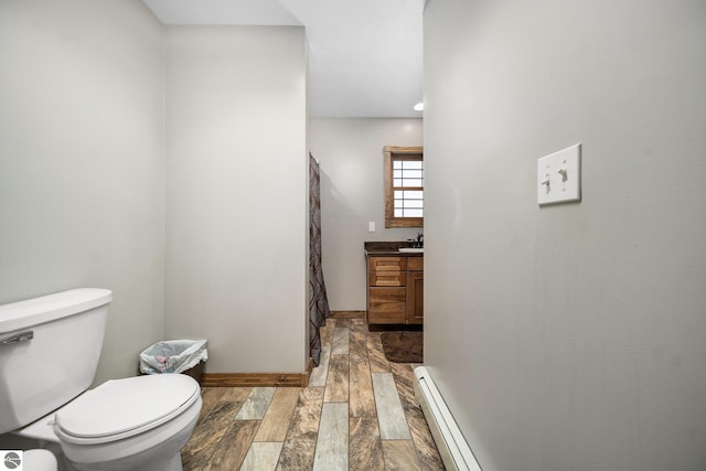 full bathroom featuring toilet, baseboard heating, vanity, wood finished floors, and baseboards