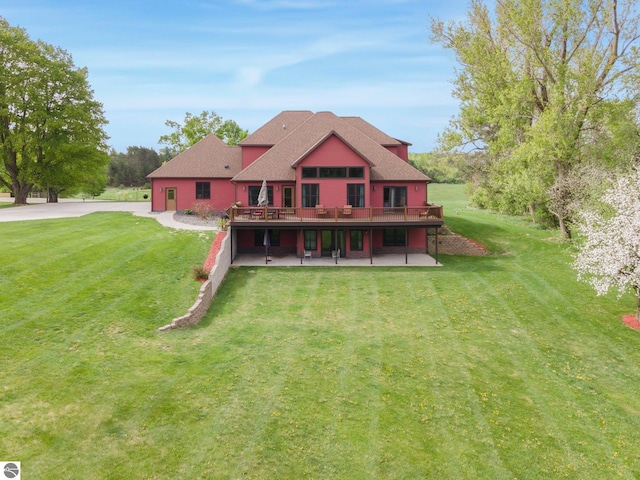 back of house with a shingled roof, a lawn, a patio area, and a wooden deck