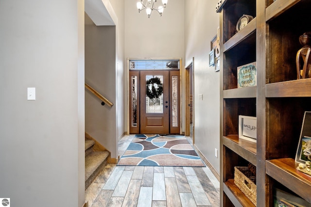 foyer entrance featuring baseboards, a towering ceiling, stairway, an inviting chandelier, and light wood-style floors