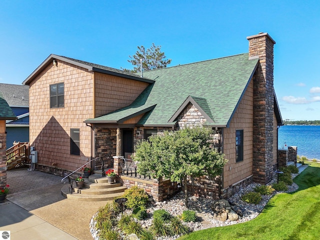 view of front of home with a water view, a shingled roof, and a chimney