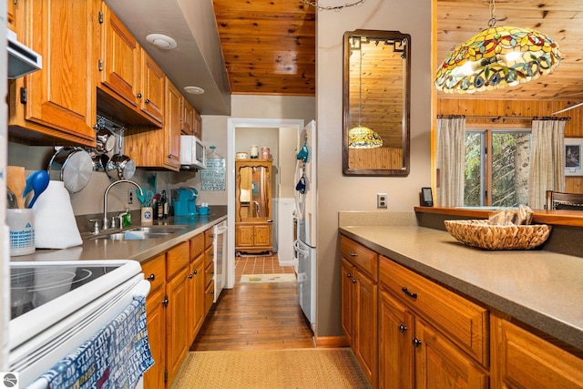 kitchen featuring decorative light fixtures, light countertops, brown cabinetry, a sink, and white appliances