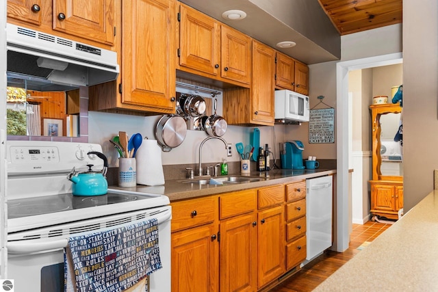 kitchen featuring white appliances, brown cabinets, light countertops, under cabinet range hood, and a sink