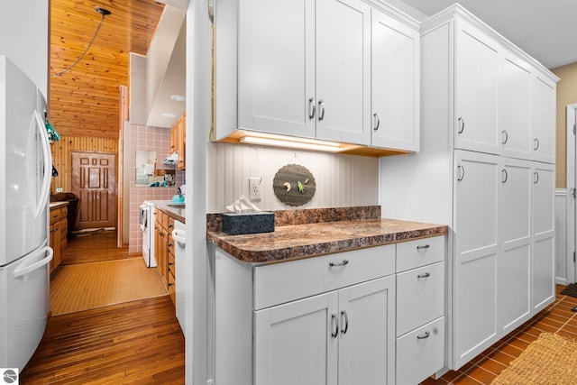 kitchen featuring dark wood-type flooring, freestanding refrigerator, white cabinetry, and dark stone countertops