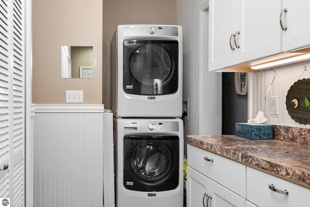 clothes washing area featuring stacked washer / dryer, wainscoting, and cabinet space