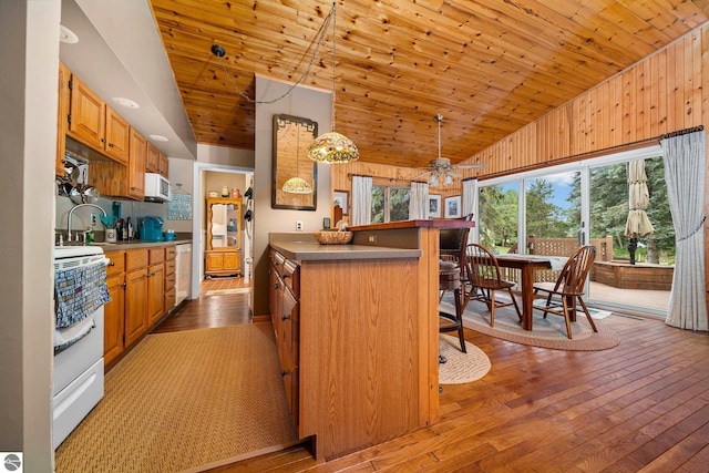 kitchen featuring pendant lighting, a breakfast bar area, dark countertops, white appliances, and hardwood / wood-style floors