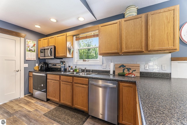 kitchen featuring stainless steel appliances, dark countertops, backsplash, a sink, and wood finished floors
