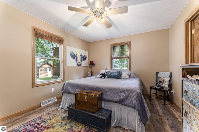 bedroom with a ceiling fan, dark wood finished floors, visible vents, and baseboards