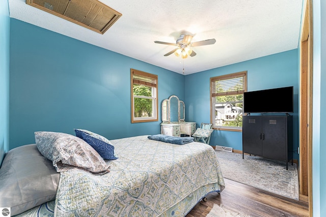 bedroom with a textured ceiling, multiple windows, wood finished floors, and visible vents