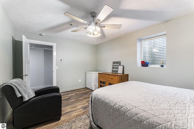bedroom with a textured ceiling, visible vents, baseboards, fridge, and dark wood finished floors