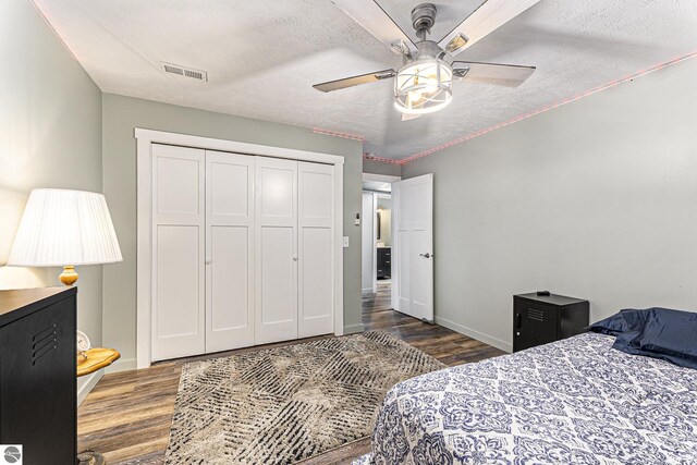 bedroom featuring dark wood finished floors, a closet, ceiling fan, a textured ceiling, and baseboards