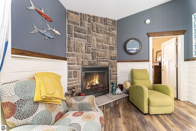 sitting room with lofted ceiling, a stone fireplace, a textured ceiling, and wood finished floors