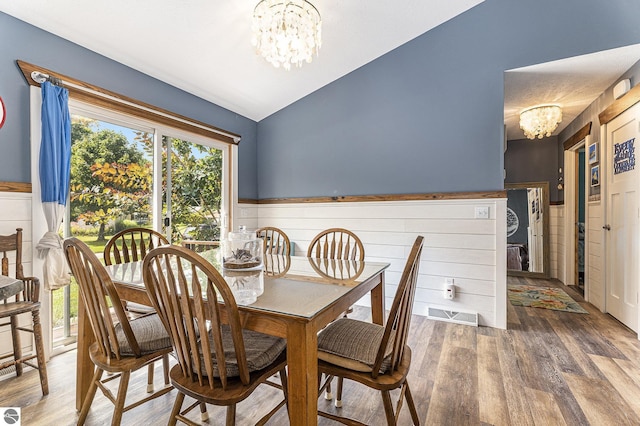 dining room with a chandelier, lofted ceiling, wainscoting, and wood finished floors
