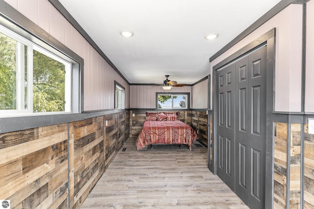 bedroom featuring recessed lighting, a closet, light wood-style flooring, ornamental molding, and wooden walls