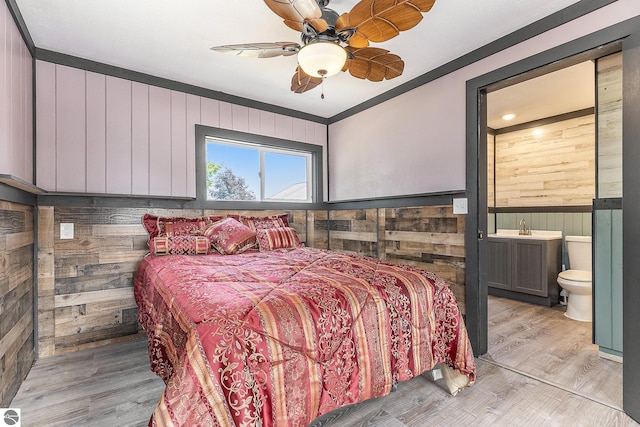 bedroom with a wainscoted wall, wood walls, light wood finished floors, and ensuite bathroom