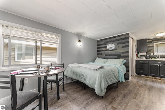 bedroom with dark wood-style floors, an accent wall, baseboards, and a sink