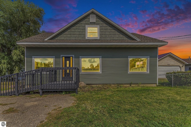 back of property with a garage, roof with shingles, a yard, fence, and a wooden deck