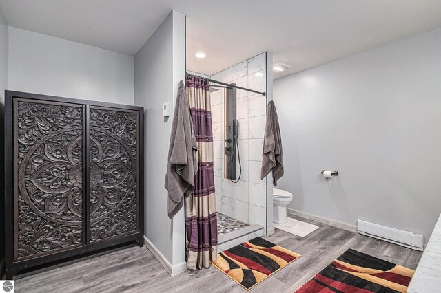 bathroom with baseboards, toilet, wood finished floors, baseboard heating, and a shower stall