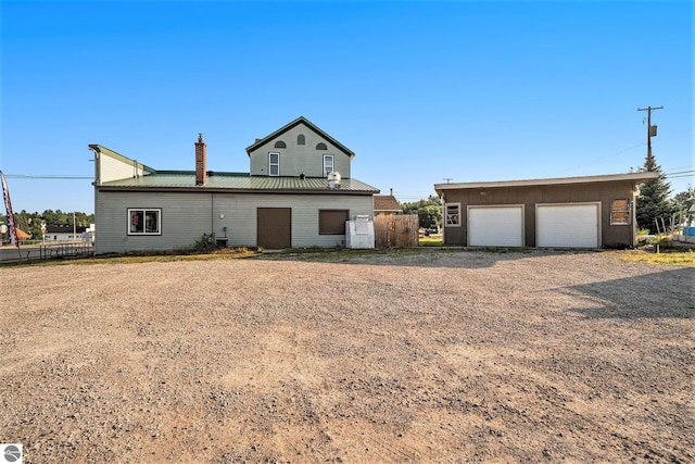 view of front facade with a garage, a chimney, metal roof, an outbuilding, and fence