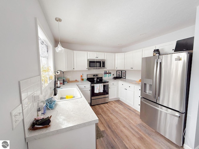 kitchen with stainless steel appliances, a sink, white cabinets, light wood-style floors, and tasteful backsplash