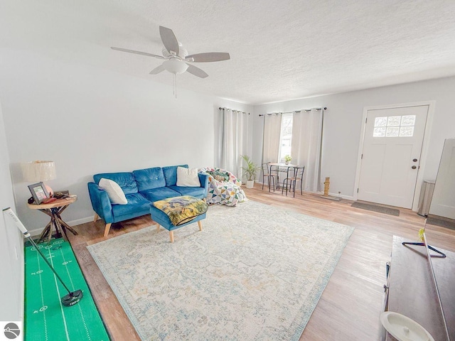 living room featuring a ceiling fan, a textured ceiling, baseboards, and wood finished floors