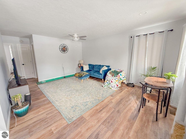 living room with a textured ceiling, ceiling fan, and light wood-style flooring