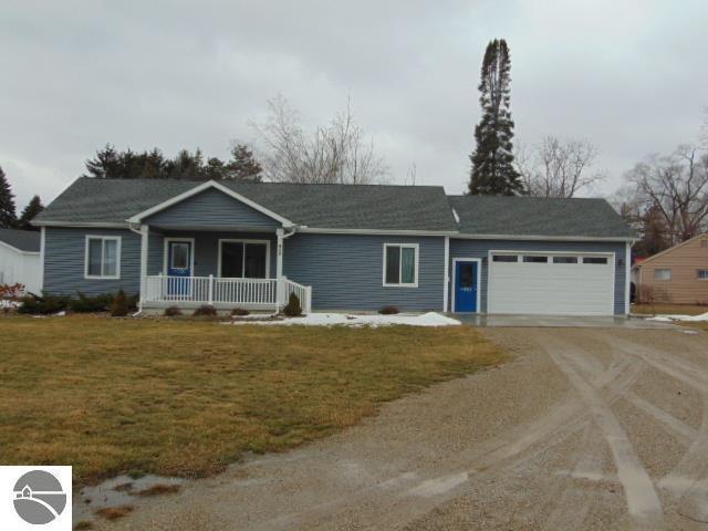 ranch-style house featuring driveway, covered porch, an attached garage, and a front lawn