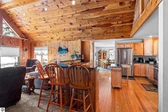 kitchen featuring wooden walls, dark countertops, appliances with stainless steel finishes, light wood-type flooring, and a sink