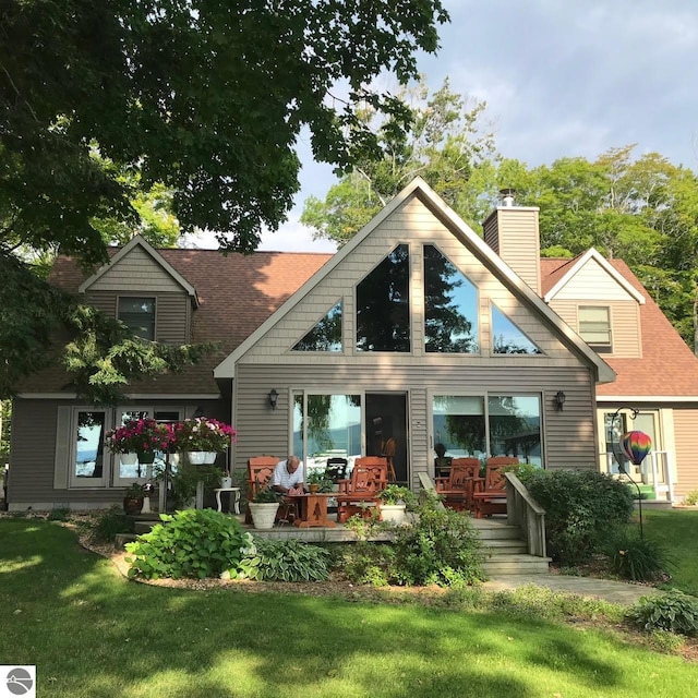 back of property featuring roof with shingles, a lawn, and a chimney